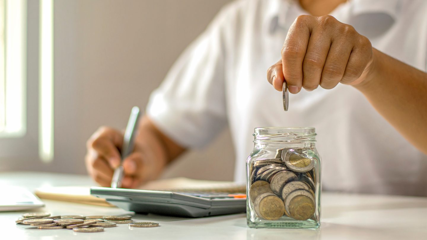 Someone adding a coin to a savings jar while working through figures
